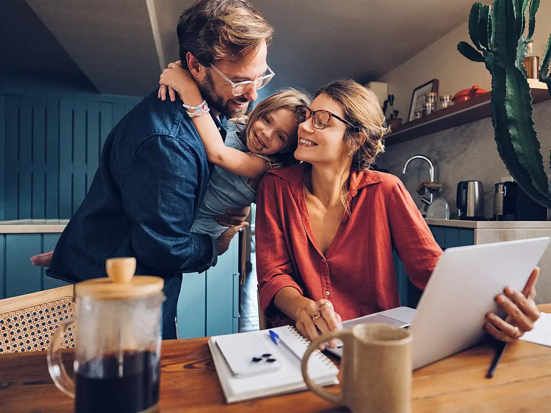 Une femme assise à une table et un homme debout derrière qui tient un enfant dans ses bras.